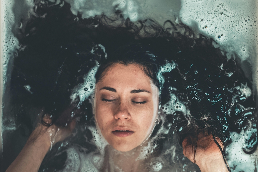 Close-up view of a woman meditating in a bathtub with eyes closed, immersed in a bubble bath.
